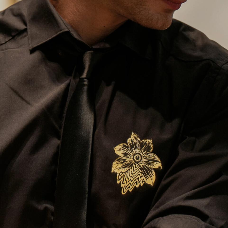 Broche en laiton doré et noir portée sur un vêtement, une chemise noire. Broche de la marque Ibride